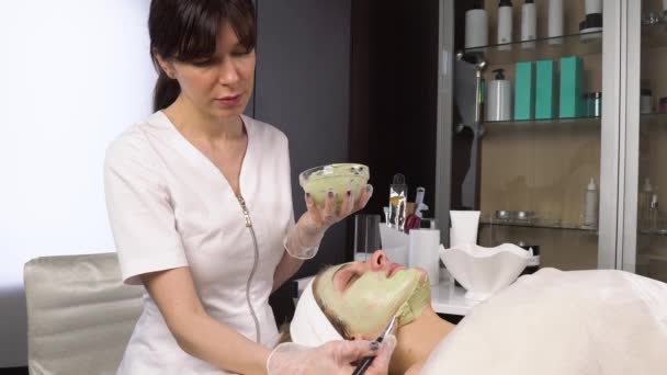 Le cosmétologue nettoie le visage avec un masque d'argile verte. Soins du visage. — Video