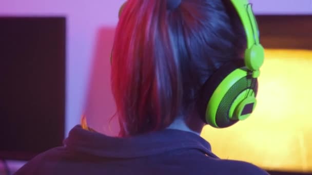 Egy fiatal nő hátradől és online játszik egy személyes számítógépen fejhallgatóval.. — Stock videók