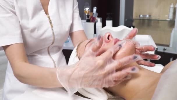 Cosmetologue une femme applique un masque cosmétique avec ses mains et fait un massage. — Video