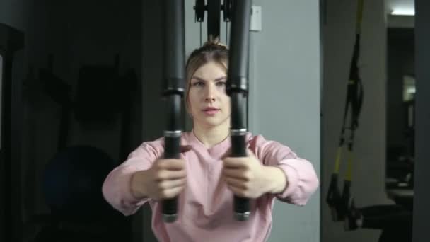 Een jonge vrouw is bezig met een simulator voor de borstspieren en armen. — Stockvideo