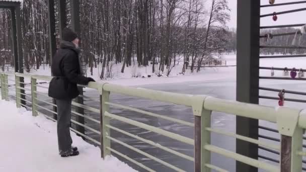 Mladá žena stojí na mostě a má výhled na zamrzlou řeku. — Stock video