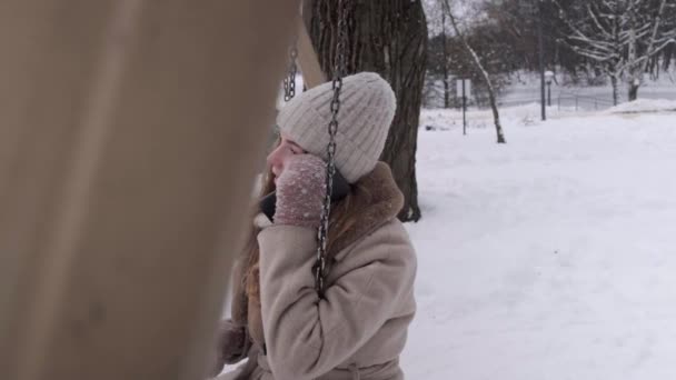 Vista lateral de uma mulher em um balanço no inverno, falando em um smartphone. — Vídeo de Stock