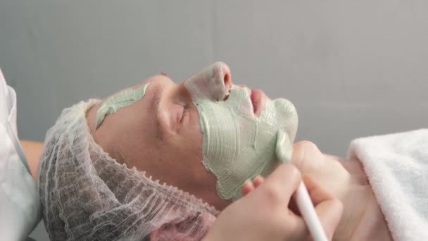 Die Kosmetikerin trägt mit einem Pinsel ökologischen Ton auf das Gesicht auf. — Stockvideo