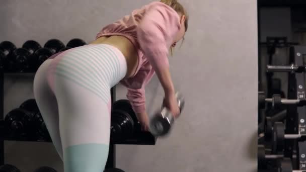 Uma vista das costas de uma mulher em roupas esportivas com halteres em suas mãos. — Vídeo de Stock