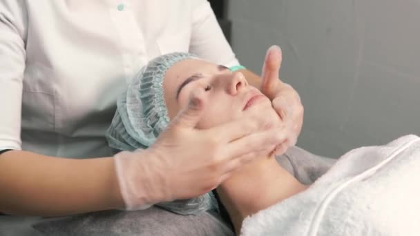 Ruce kosmetologa v rukavicích dělají masáž obličeje klienta. — Stock video
