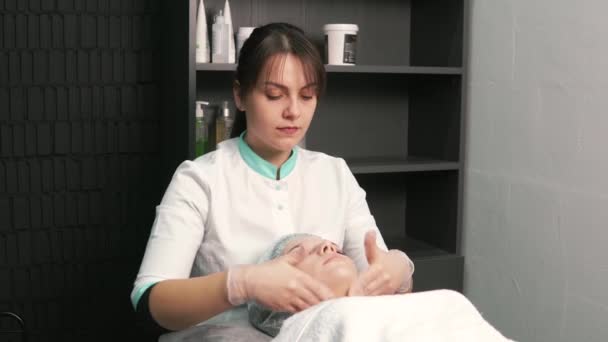 De cosmetoloog in handschoenen doet een gezichtsmassage van de cliënt. Schoonheidssalon. — Stockvideo