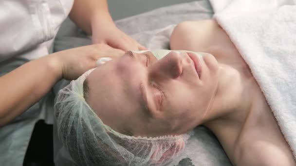 Kvinnlig kosmetolog händer rengöra ansiktet på en ung man med en servett. — Stockvideo
