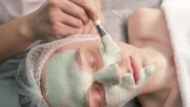 Un cosmétologue applique de l'argile écologique sur le visage dans un salon de beauté. — Video