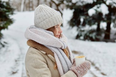 Eldivenli bir bardak sıcak içecekle örülmüş şapkası olan genç bir kadın..