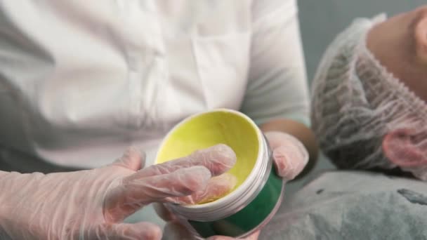 Les mains d'une cosmétologue prennent une crème hydratante jaune dans un bocal. — Video