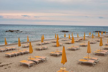 Boş güneş yatakları ve turuncu şemsiyeli sarı kumsal. Gün batımı gökyüzü.