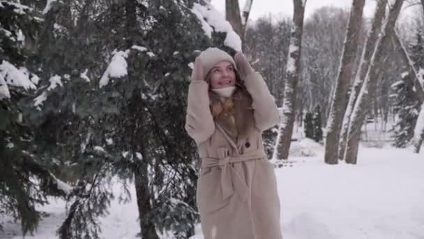 Uma bela mulher cobre seu rosto da queda de neve com suas mãos mitenadas. — Vídeo de Stock