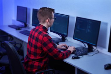 Kırmızı ekose gömlekli genç bir adam monitöre bakıyor. Ofiste çalış..