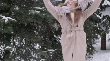 A blonde woman throws snow up in pink mittens. A cold, snowy winter.