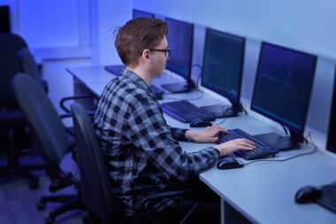 Gözlüklü bir öğrenci ofiste monitörün önünde ders çalışıyor..