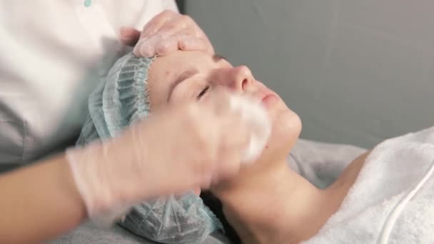 Kozmetik uzmanı, genç bir bayan müşterinin yüzünü bez peçeteyle temizliyor.. — Stok video