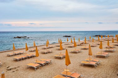 Güzel, boş güneş yatakları ve turuncu şemsiyeli sarı kumlu boş bir sahil..