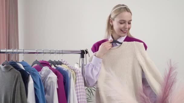 Una blogger estilista rubia se prueba la ropa y mira a la cámara. — Vídeos de Stock