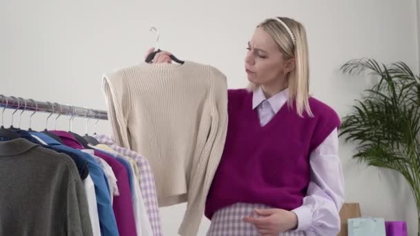 Una estilista femenina muestra la ropa en sus manos, el concepto de elección. — Vídeos de Stock