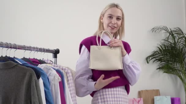 Una estilista femenina muestra un elegante bolso ligero, sonríe y mira a la cámara. — Vídeos de Stock