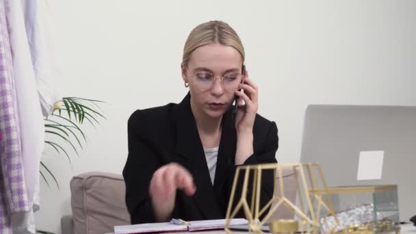 Seorang wanita muda stylist dalam jaket hitam berbicara pada smartphone dengan klien — Stok Video
