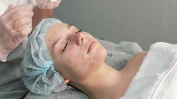 El cosmetólogo aplica una crema hidratante blanca en la cara. Salón de belleza. — Vídeo de stock
