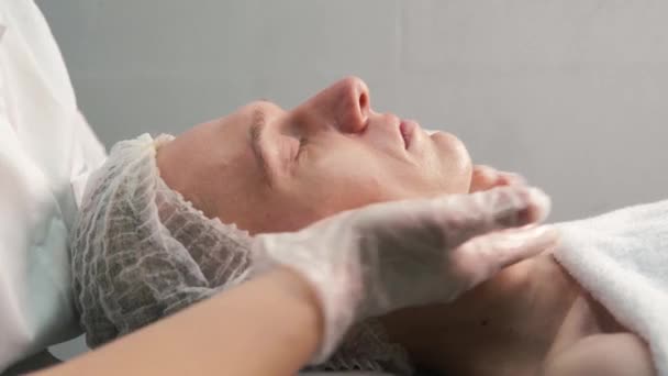 Косметолог з рукавичками дає масаж обличчя молодому чоловікові . — стокове відео