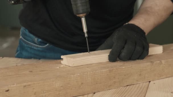 A young man screws a self-tapping nail into a wooden board with a drill. — Stock Video