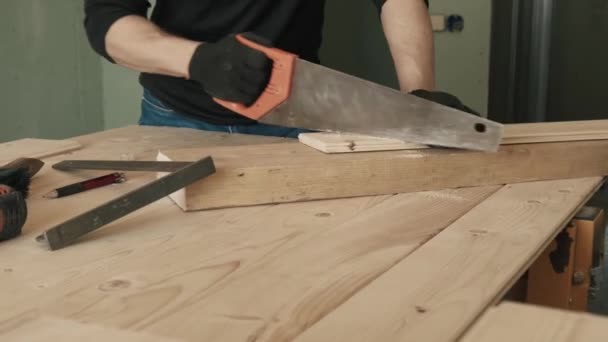 Samec stavebního dělníka pilou na ruce piluje dřevěnou desku. Video 4k. — Stock video