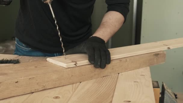 Mężczyzna budowlaniec używa wiertarki do robienia dziury w drewnianej desce.. — Wideo stockowe