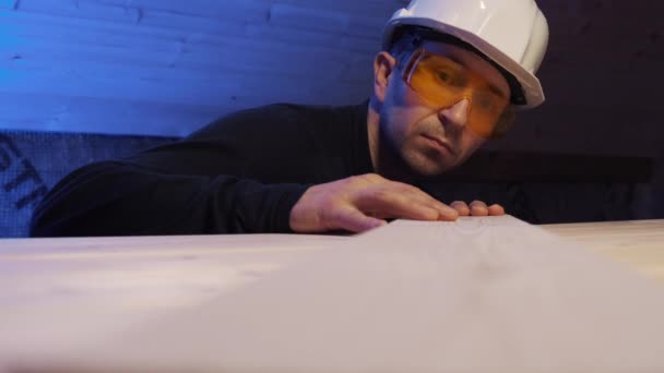 En byggarbetare i hjälm och glasögon kör handen över brädet. — Stockvideo