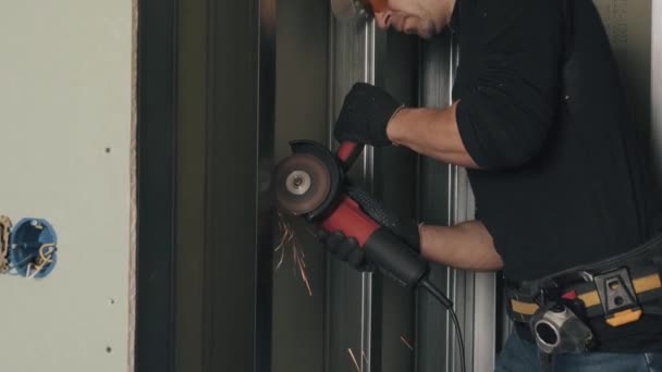 Um homem trabalha com um moedor de ângulo, um trabalhador da construção civil com um chapéu duro. — Vídeo de Stock