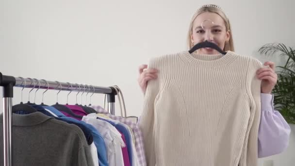 Egy szőke női stylist ruhákat próbál fel, mosolyog és a kamerába néz.. — Stock videók