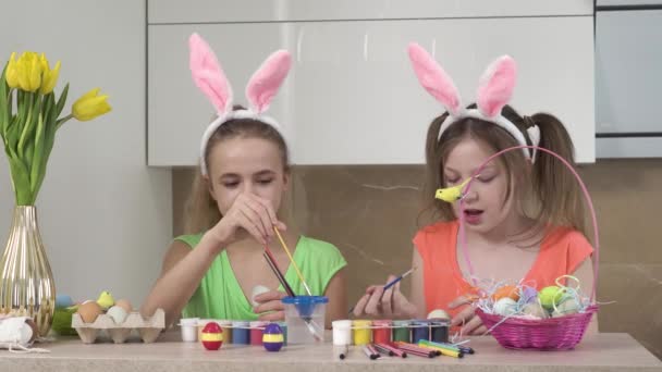 Dos hermanas están decorando huevos de Pascua en la cocina. Vacaciones de Pascua. — Vídeos de Stock
