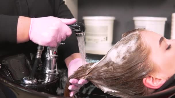 Перукар в рукавичках миє шампунь від клієнтського волосся в умивальнику — стокове відео