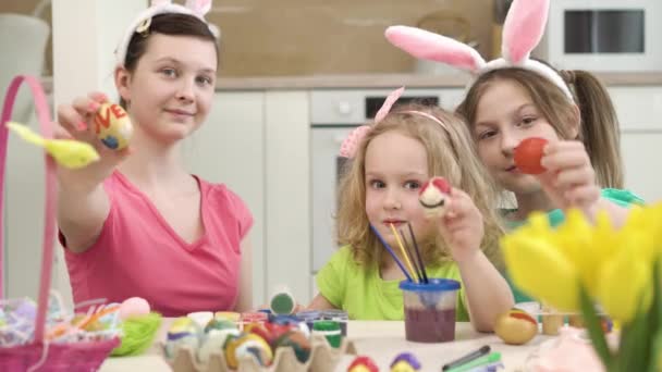 Три красиві дівчата показують малюнки на великодніх яйцях перед камерою . — стокове відео