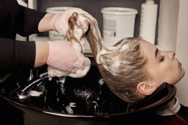 Vista lateral do cabeleireiro mãos ensaboando o cabelo do cliente com xampu. Fotos De Bancos De Imagens
