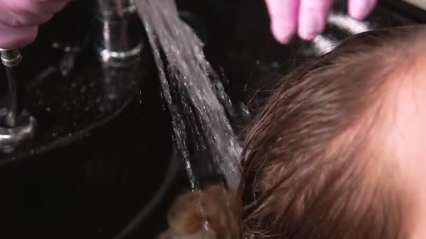 Detailní záběr na ruce kadeřníka mytí barviva z vlasů. — Stock video