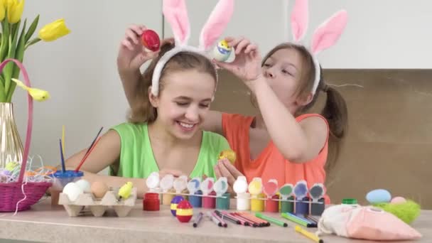 Två söta flickor leker med dekorerade påskägg. Kaninöron på huvudet. — Stockvideo