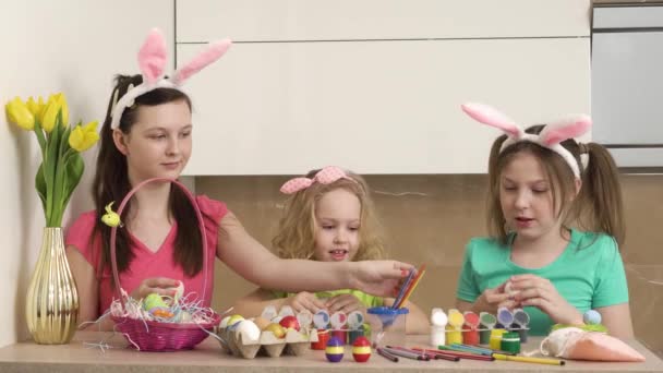 Tres hermosas chicas con orejas de conejo pintan huevos de Pascua con pintura. Vídeo 4k. — Vídeo de stock