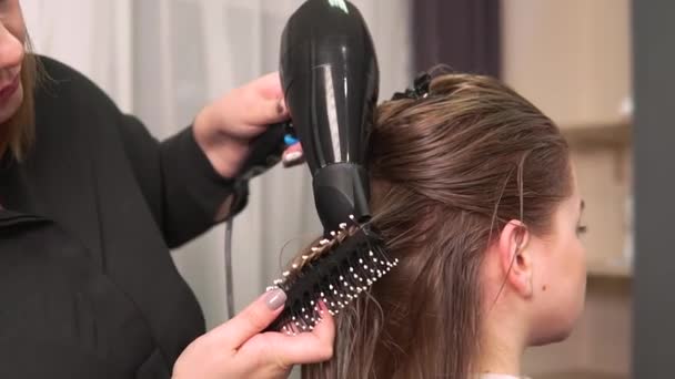 Le coiffeur sèche les cheveux raides avec un sèche-cheveux et les peigne avec un peigne. — Video