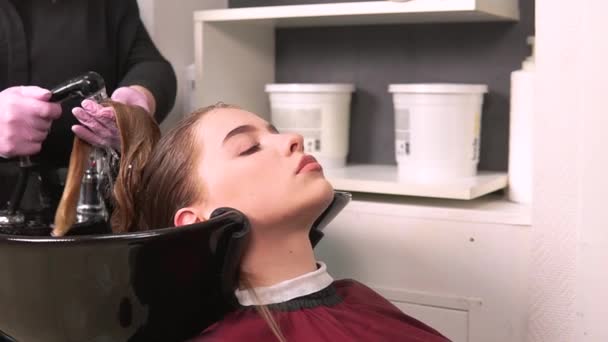 Una peluquera con guantes lava el cabello de un cliente rubio en un lavabo negro. — Vídeo de stock