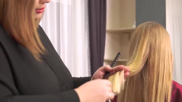 Une femme coiffeuse coupe les extrémités des cheveux blonds naturels avec des ciseaux. — Video