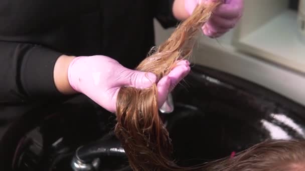 Una peluquera aplica una mascarilla hidratante al cabello húmedo de una mujer rubia. — Vídeos de Stock