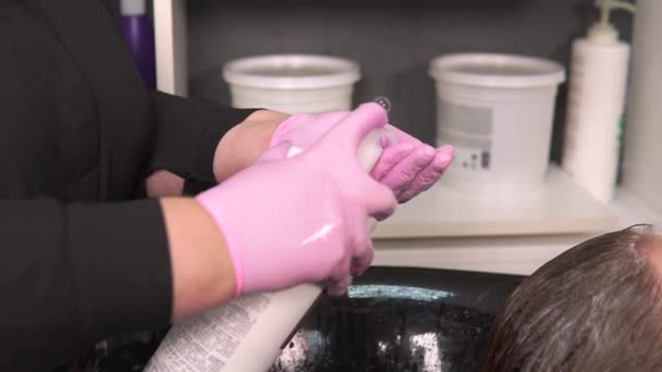 En handske frisör plockar upp schampo från en burk. Professionell hårvård. — Stockvideo