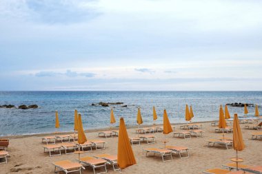 Boş güneş yatakları ve turuncu şemsiyeli kıyı şeridi.