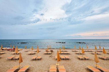 Güneşli yatakları ve parlak turuncu şemsiyeleri olan güzel boş bir sahil..