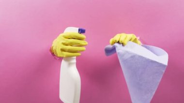 Hands in a rubber yellow glove holding a cloth and spray for washing windows.