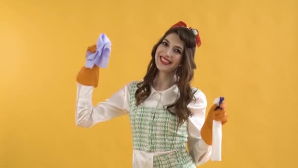 Una mujer positiva baila con guantes de goma con spray y un trapo. Fondo amarillo — Vídeos de Stock