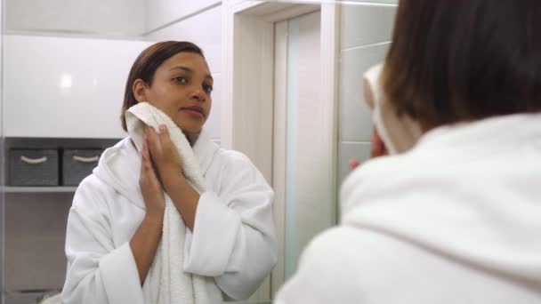 Une jeune belle femme se regarde dans le miroir et essuie son visage avec une serviette. — Video